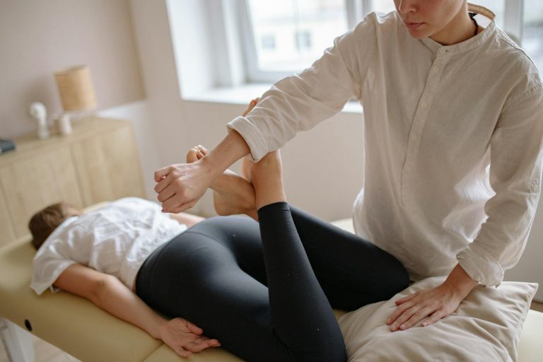 A therapist performs a leg adjustment on a client lying face down in a clinic setting.